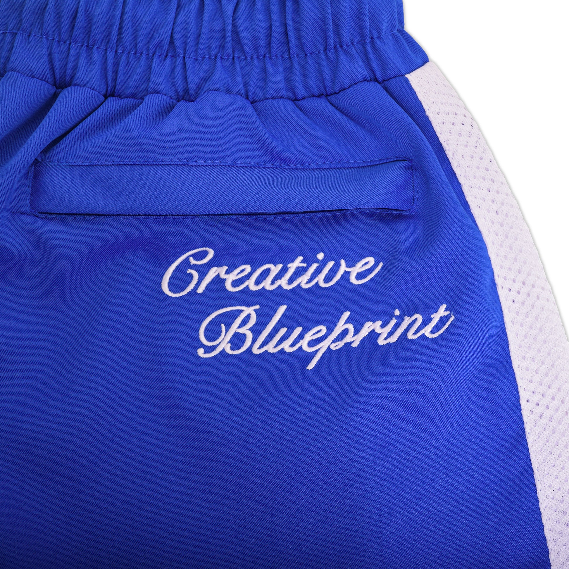 An up-close view of the upper back pocket on the Nylon Track Pants with white, cursive Creative Blueprint embroidery on top of the hidden pocket.