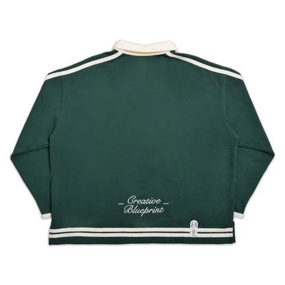 A full back view of our forest green Inner Child Rugby shirt. The same cream striping is present on the back view with a single embroidery hit centered at the bottom of the garment, just above the stripes, spelling "Creative Blueprint" in a script font. The cream collar is also visible at the top of the photo.