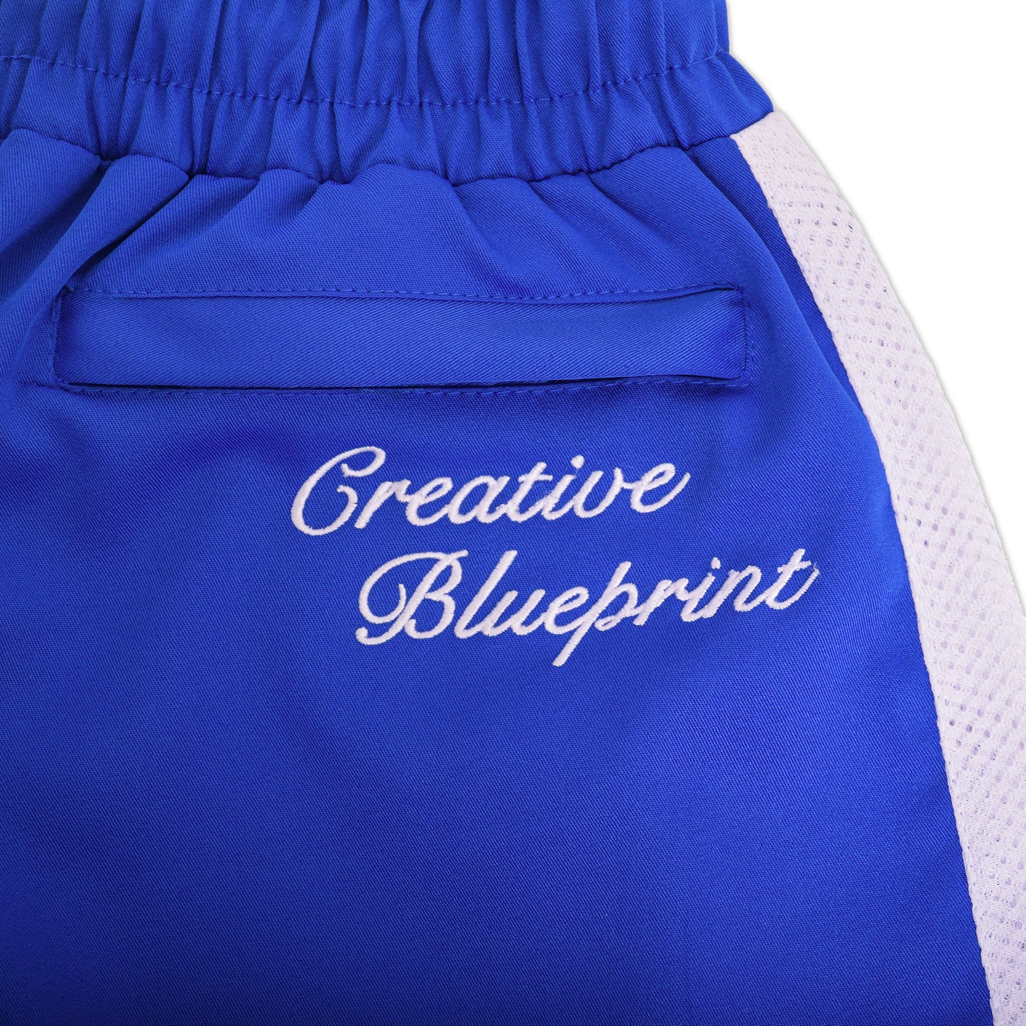 An up-close view of the upper back pocket on the Nylon Track Pants with white, cursive Creative Blueprint embroidery on top of the hidden pocket. 