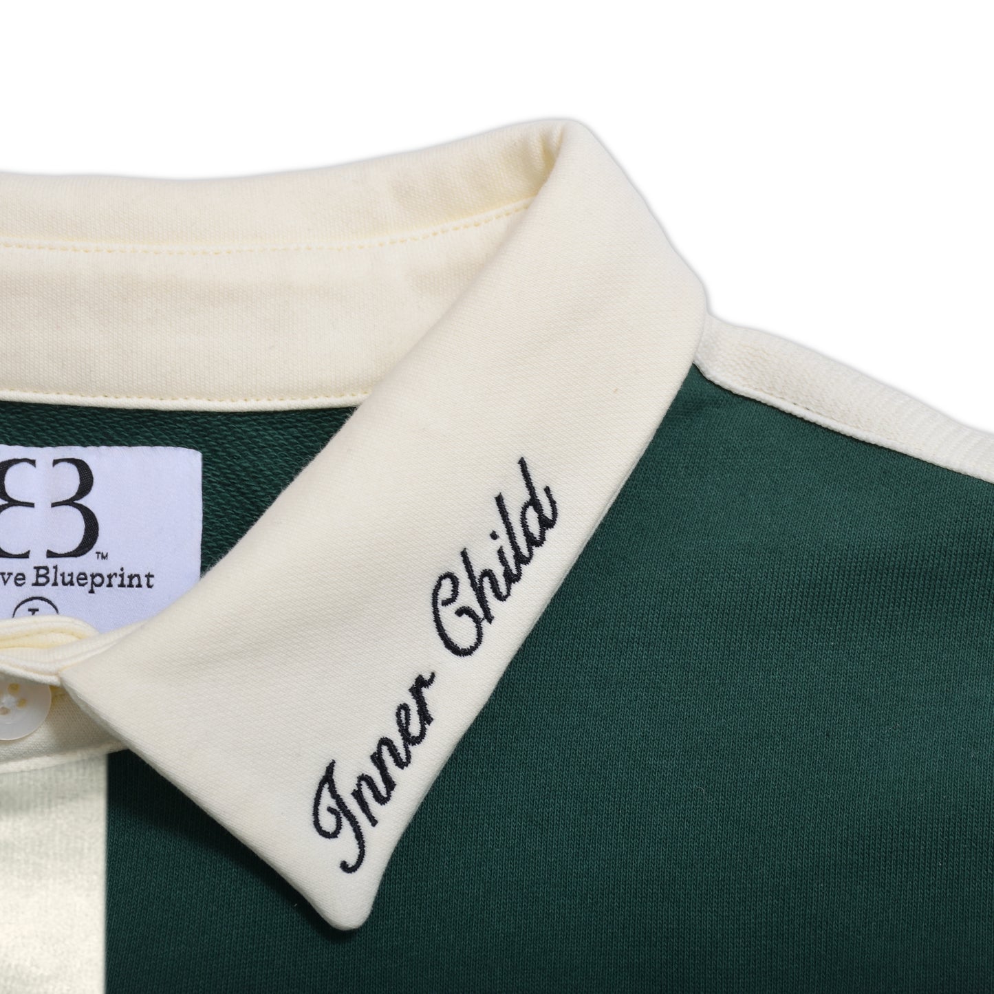 An up-close view of the left side of cream collar on the shirt. "Inner Child" is embroidered on the collar, centered in the middle of the photo. The custom woven neck label and ribbon of the fabric holding the buttons is slightly visible on the left side of the image.