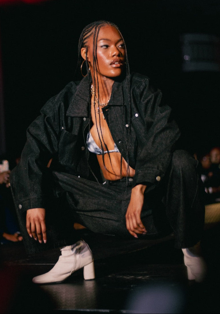 Model on a fashion runway wearing a black coat and white shoes.