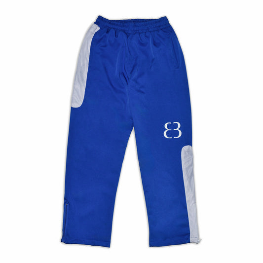 Full front view of the Nylon Track Pants in imperial blue with the pant legs fully extended, showcasing the asymmetrical side white mesh panels and knee level logo screen print.